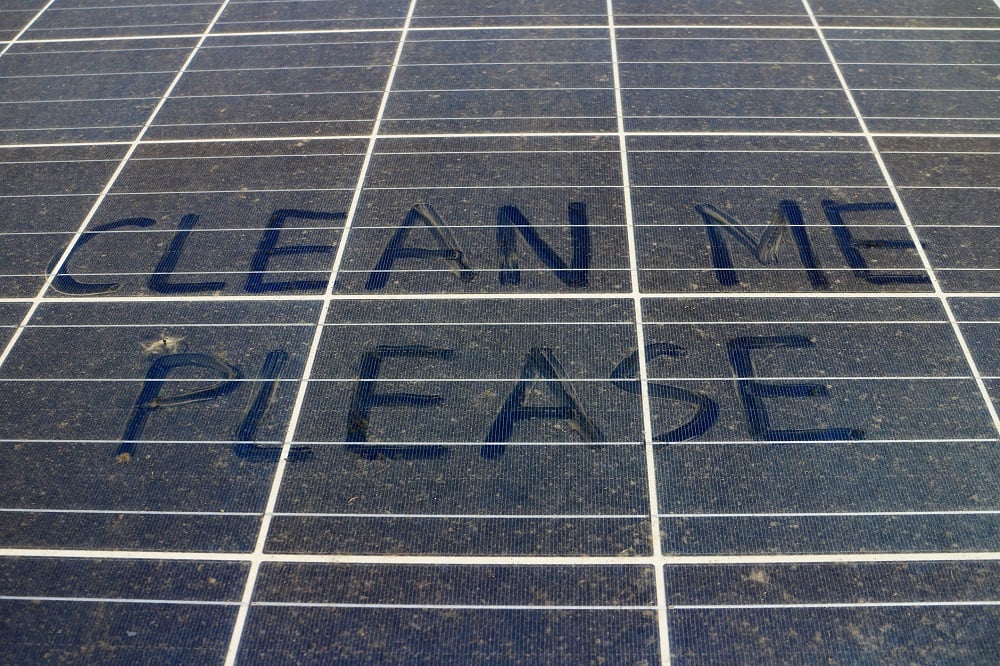 Solar panel with clean me please written in the dust that covers it.