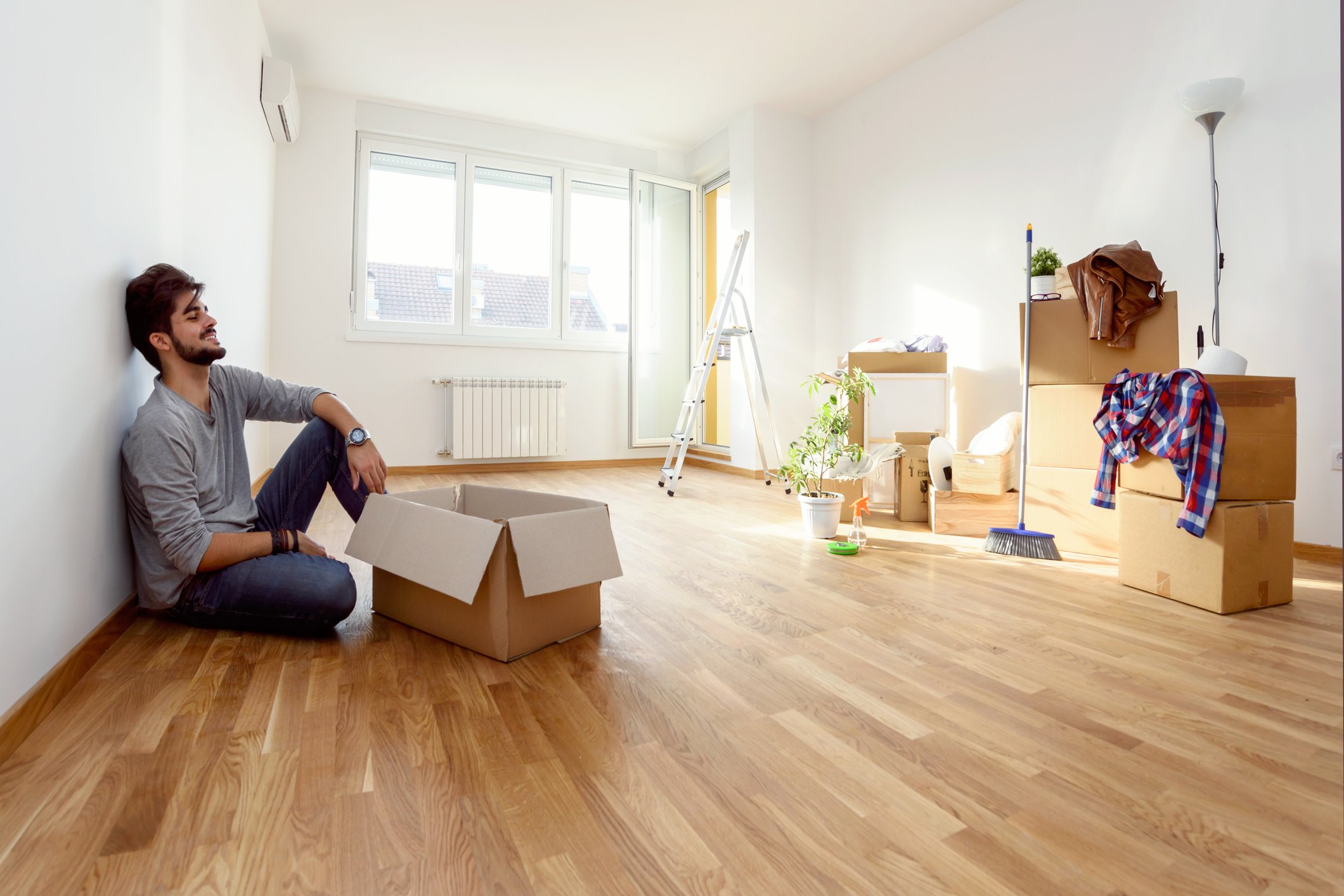 Young man sitting on floor next to a moving box, while other boxes are stacked across the room.