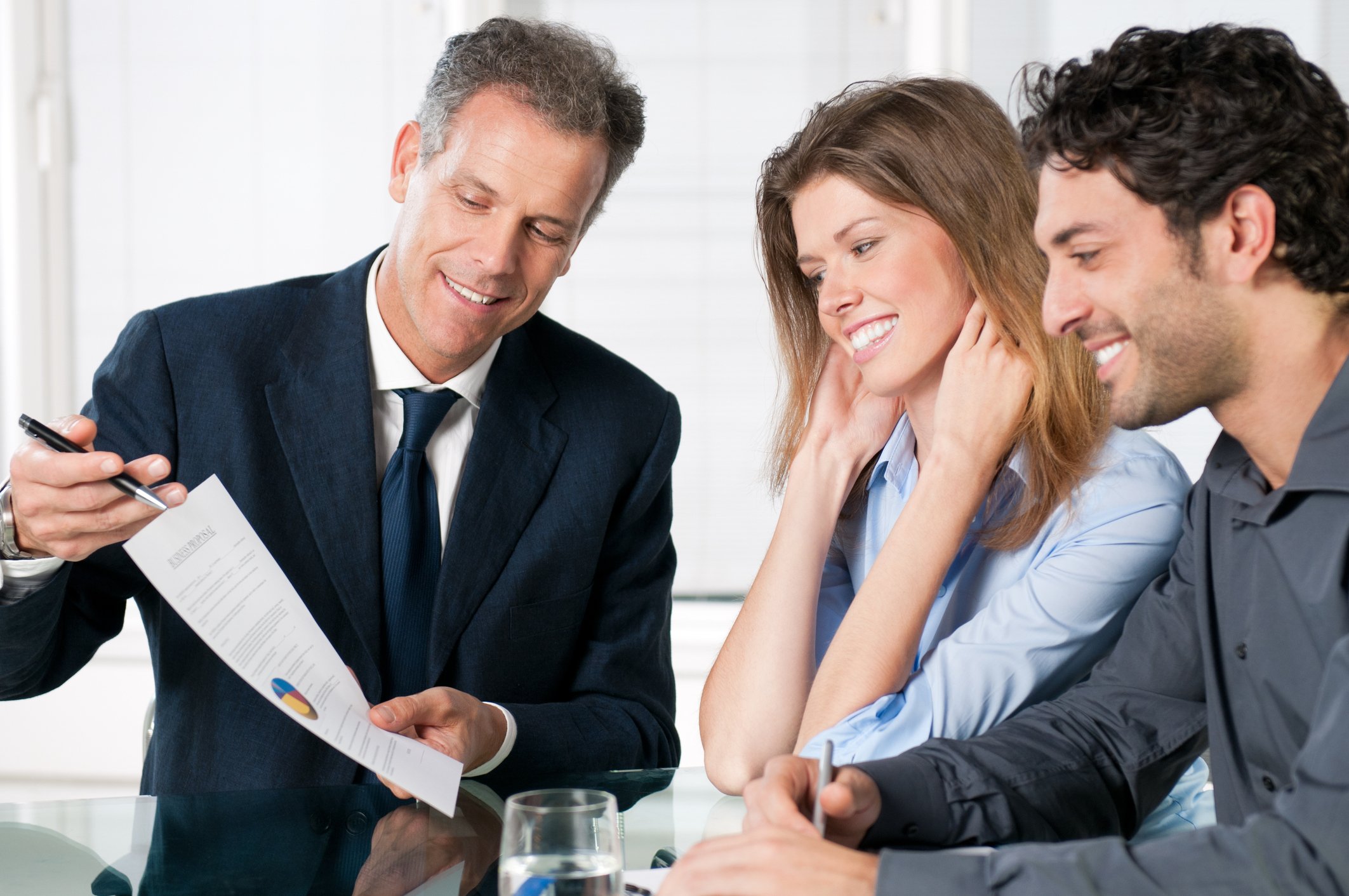 Man in suit presenting document to smiling young couple.