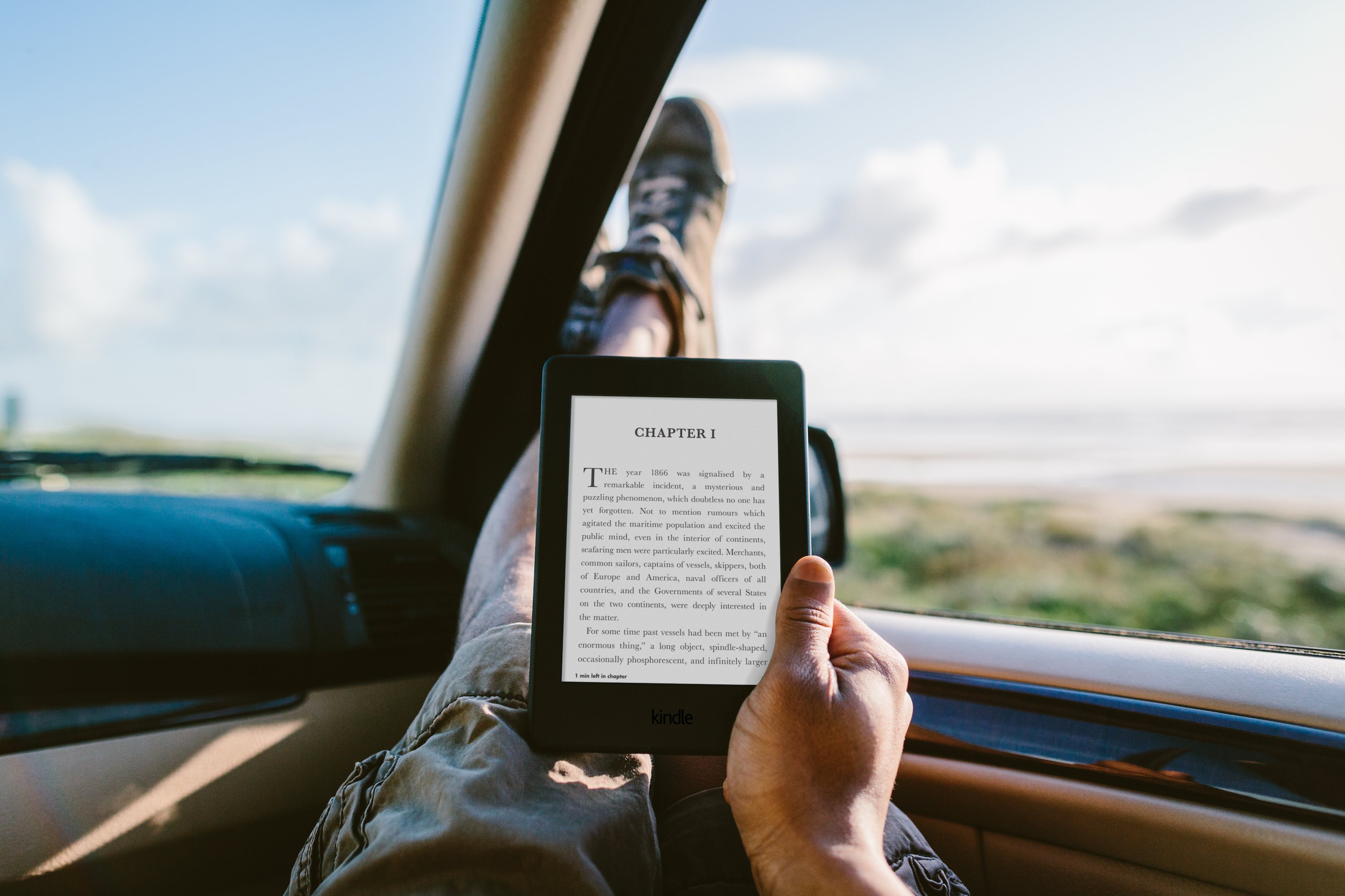 A hand holding a Kindle Paperwhite in a car.