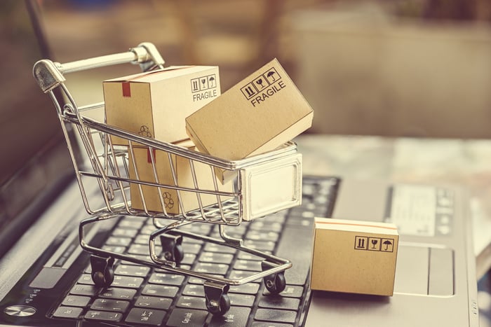 A small toy shopping cart full of boxes sits on a laptop