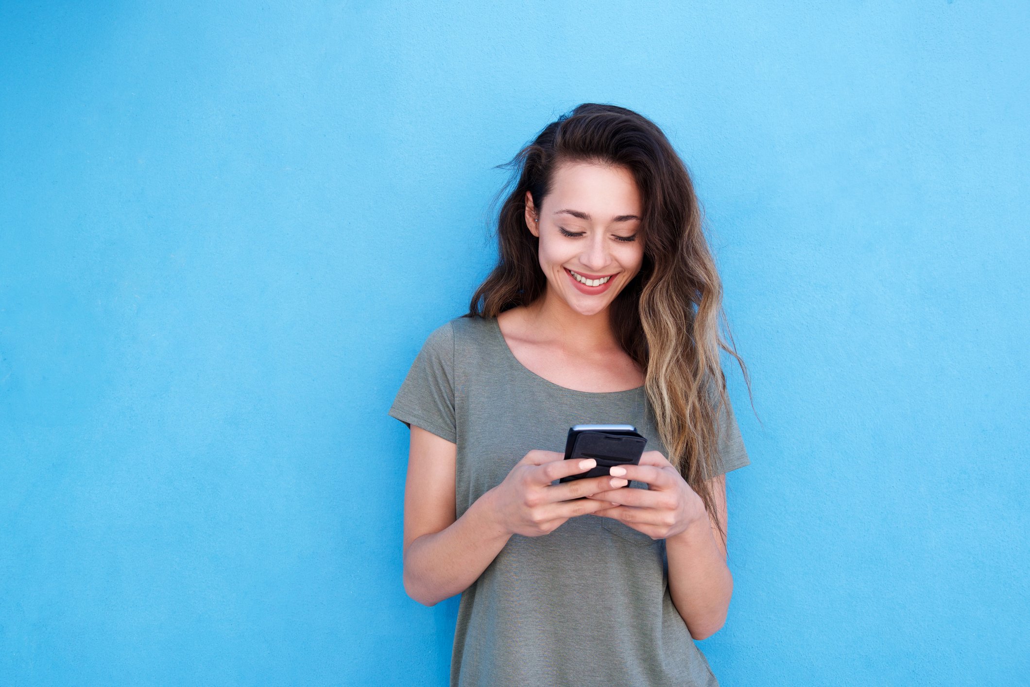 Woman on smartphone standing against a blue wall.
