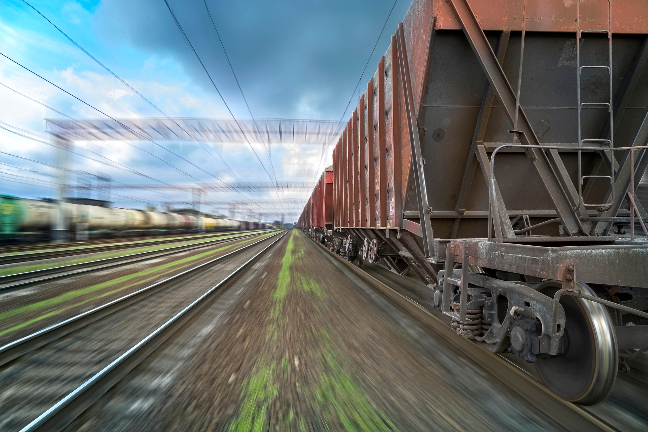 Freight train with top-loaded cars passing viewer in a blur.