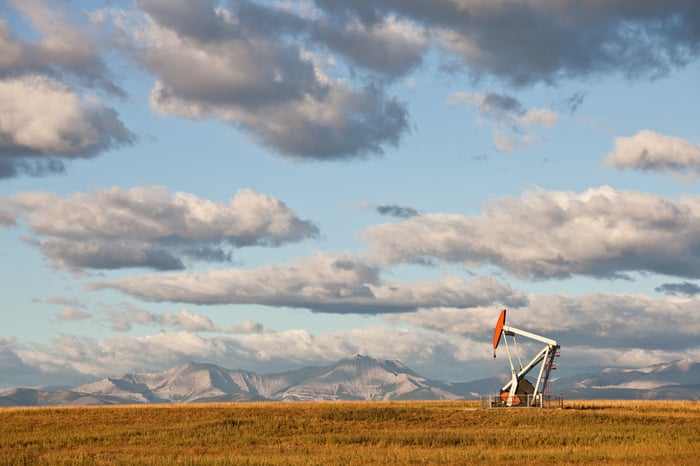 An oil pump in a field with the mountains in the background.