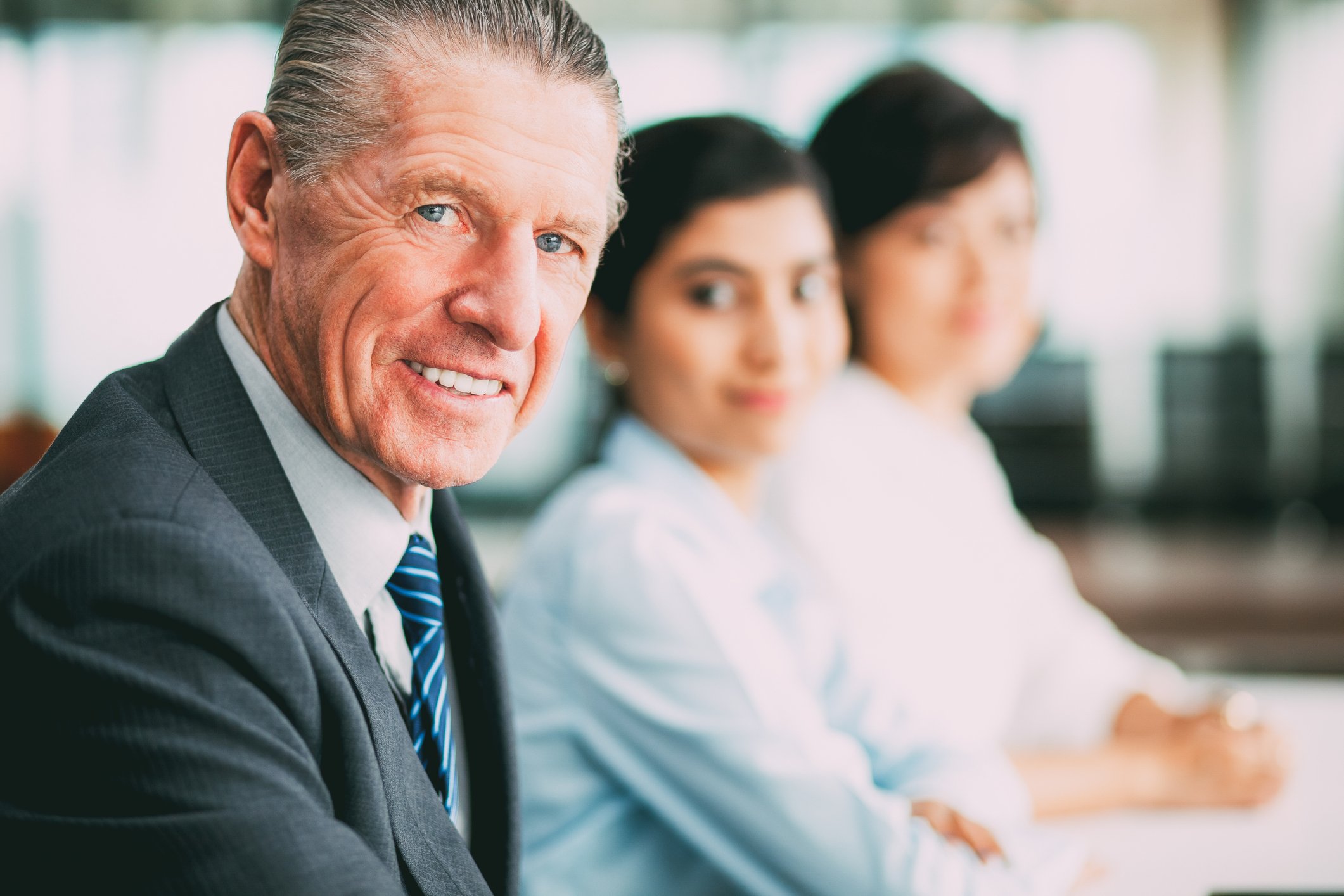 Smiling older man in suit sitting next to two younger female workers.