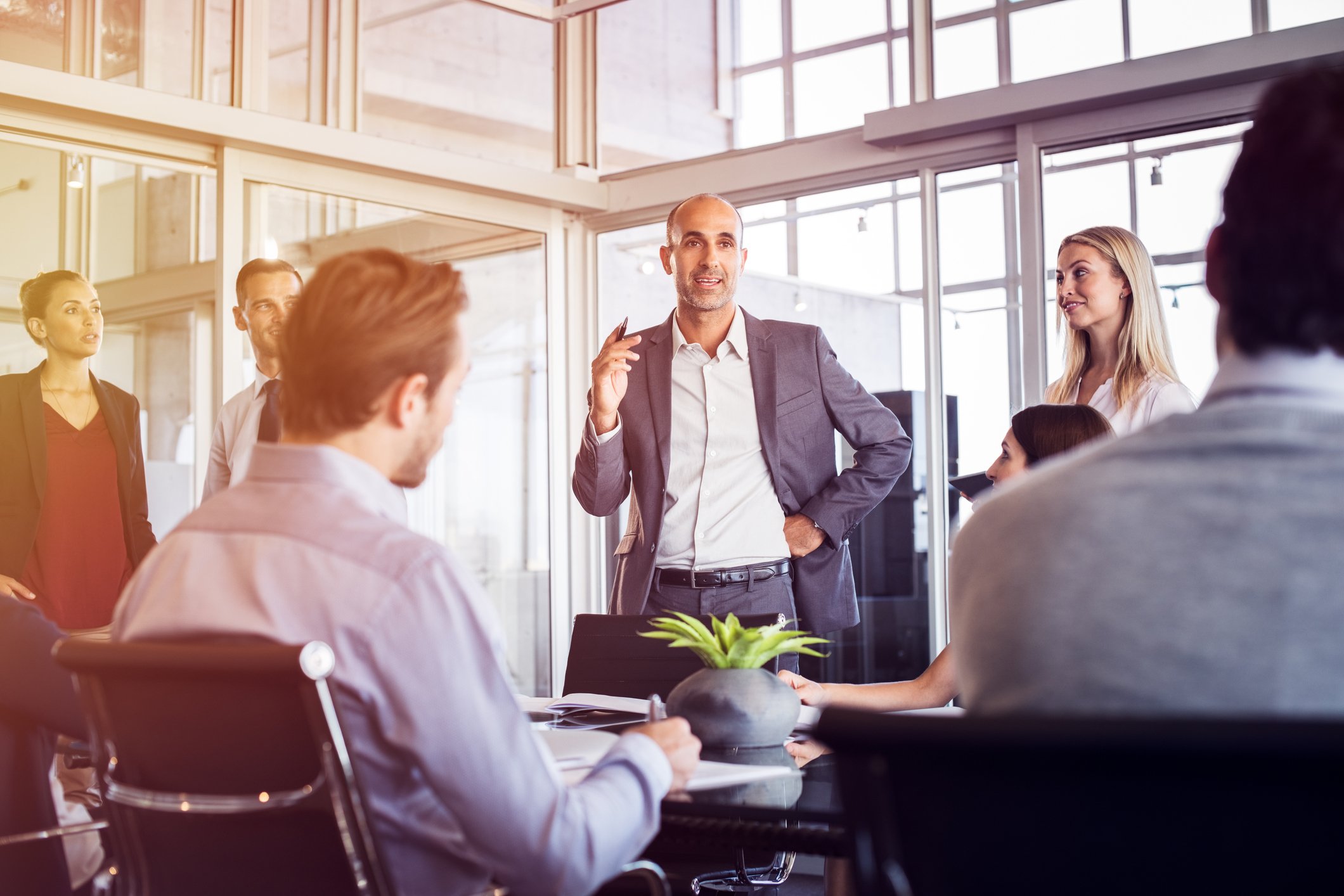Man in suit standing and talking while a group of professionals looks on