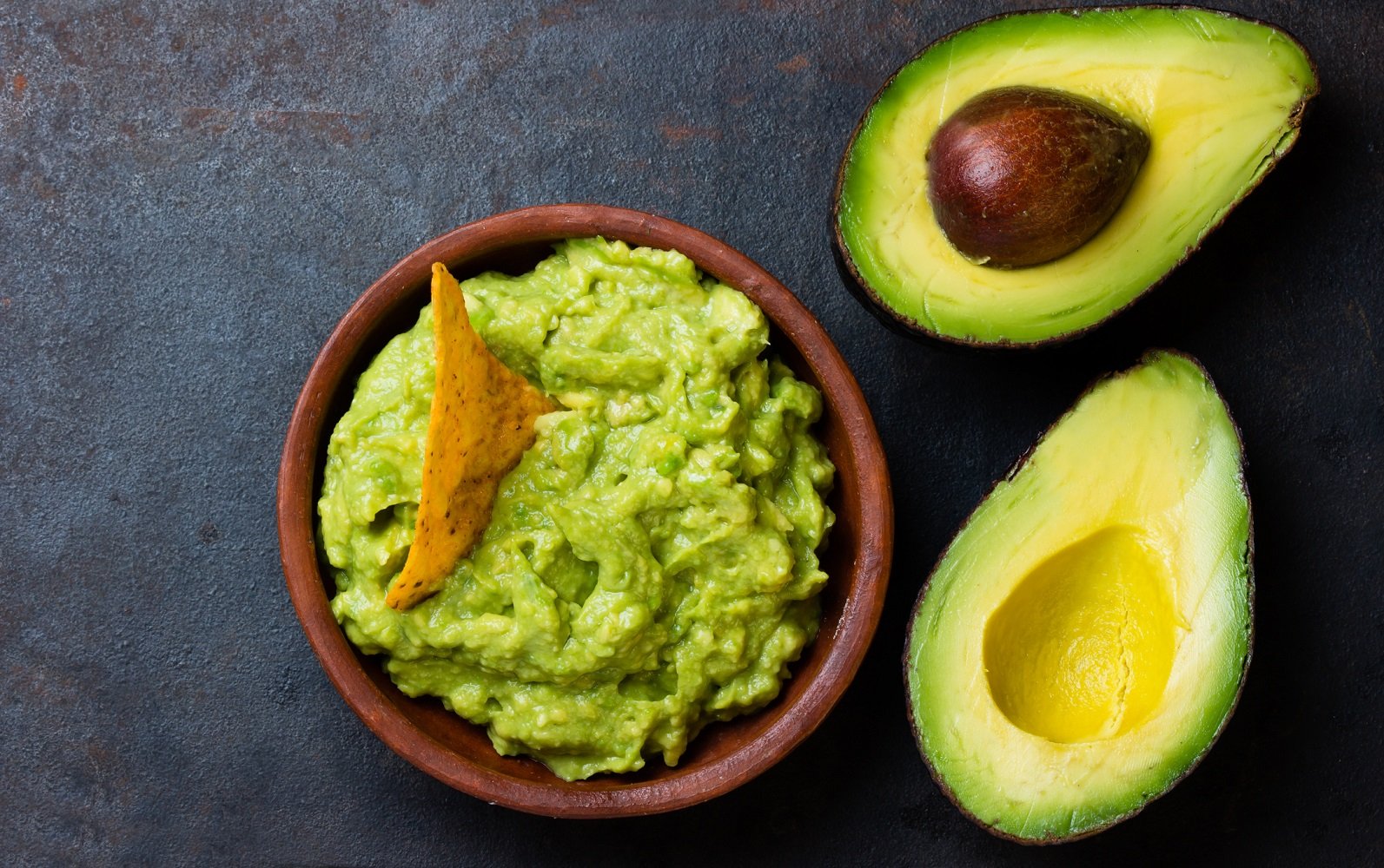 A bowl with guacamole and sliced avocados on a table. 