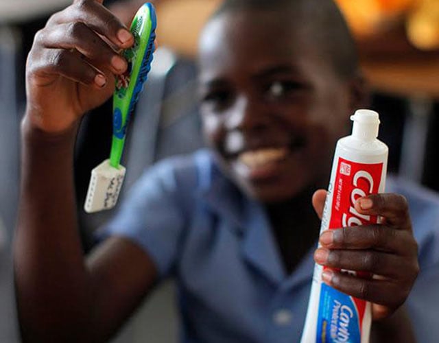 A boy holds up a tube of Colgate toothpaste and a toothbrush.