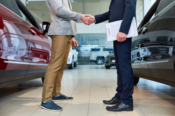 A male customer shaking hands with a car salesman.