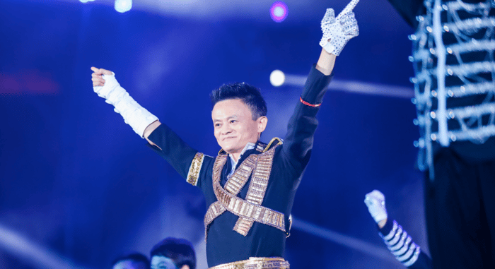 Alibaba cofounder Jack Ma lifts his arms up in victory while speaking on stage at an event.