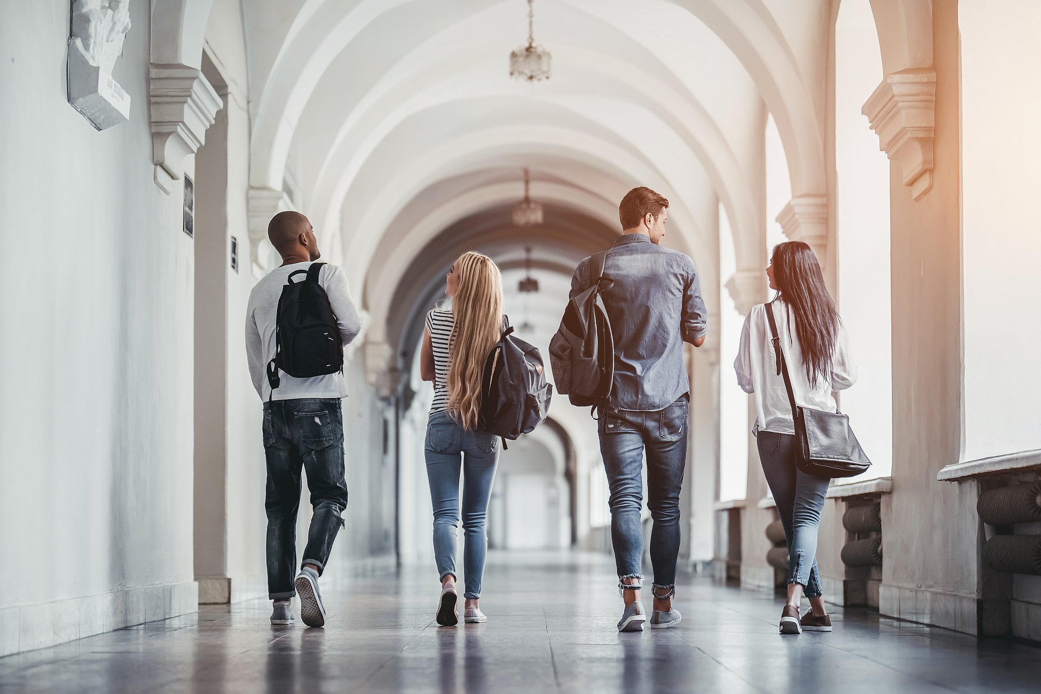 Students walking in a gothic-arched university hallway.