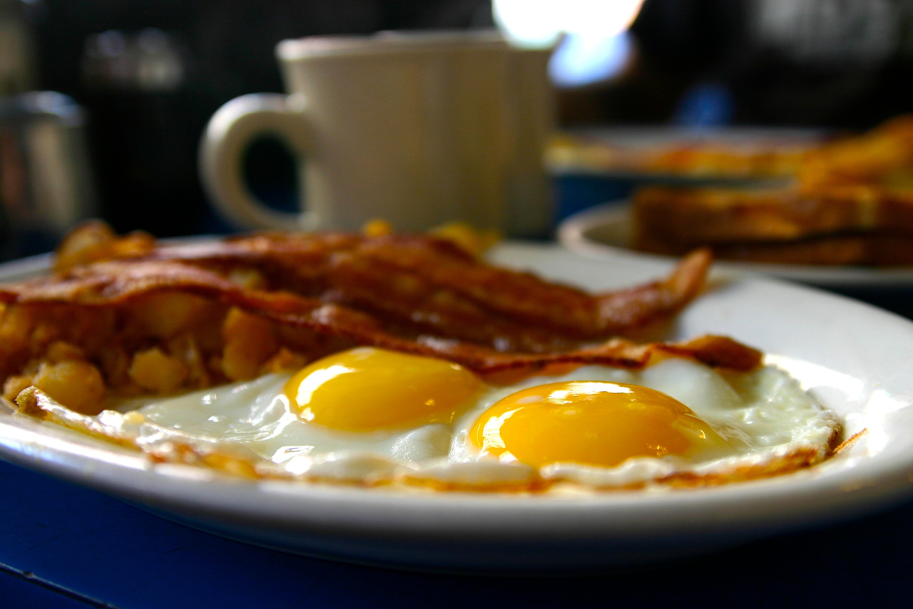 Bacon and eggs on a plate at a diner with a coffee cup in the background