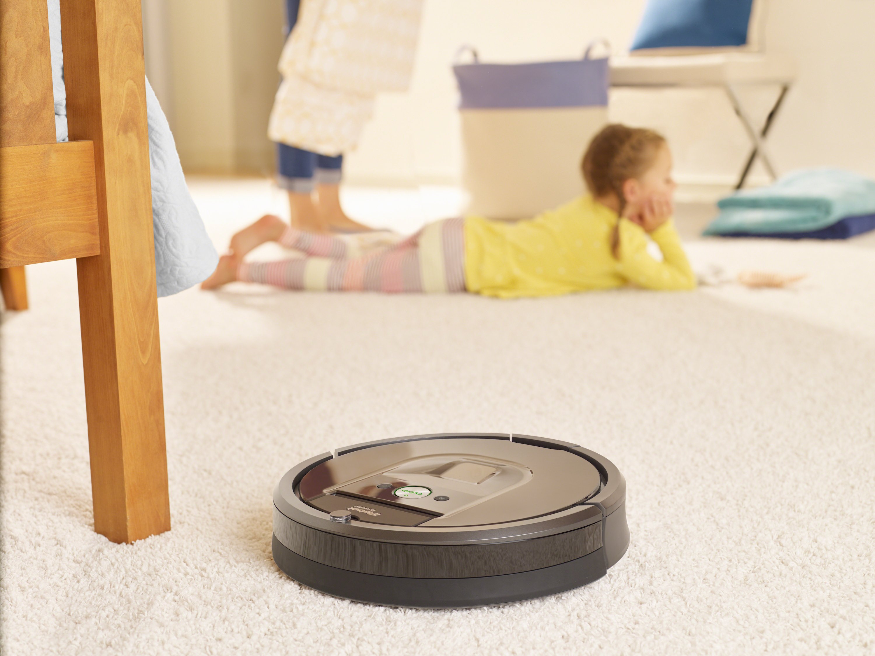 iRobot Roomba 980 cleaning carpet in a home, while a child lies on the floor nearby.