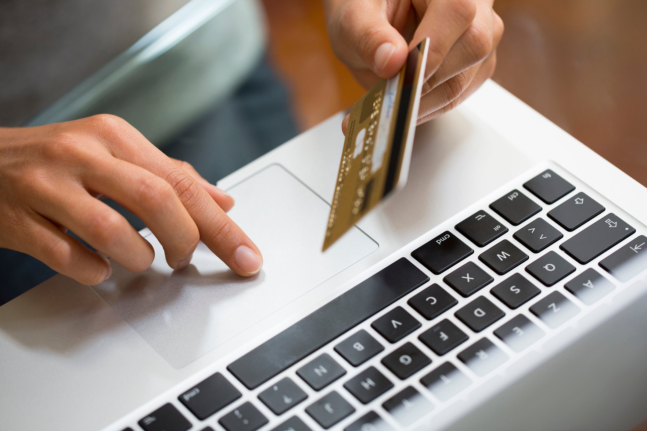 A person holds a credit card over a laptop keyboard.