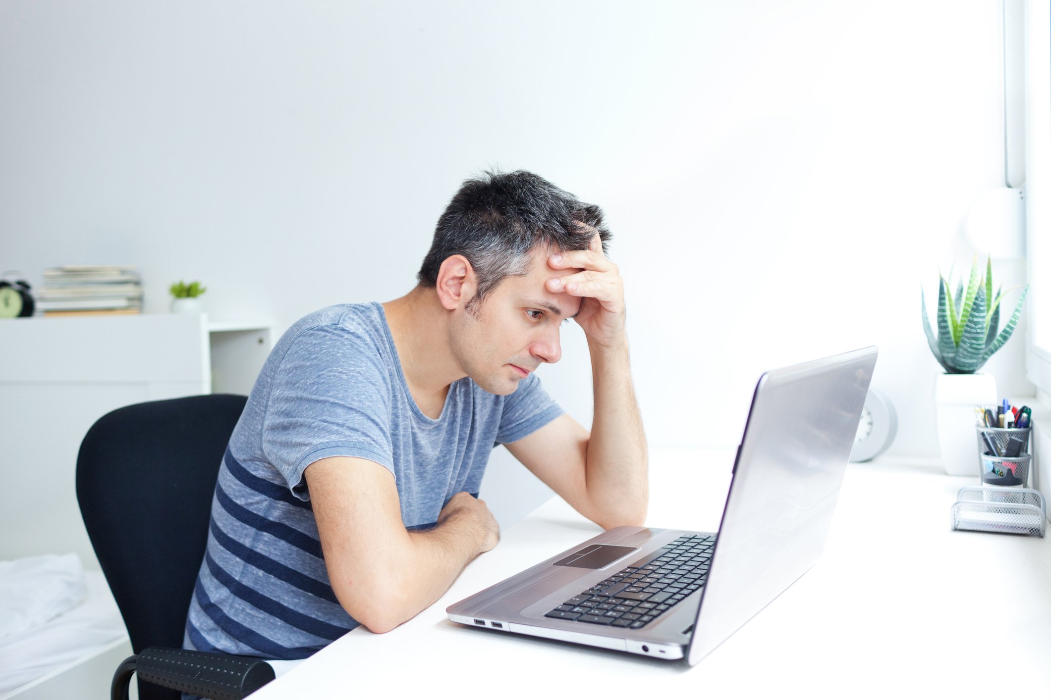 Man at laptop holding his head.