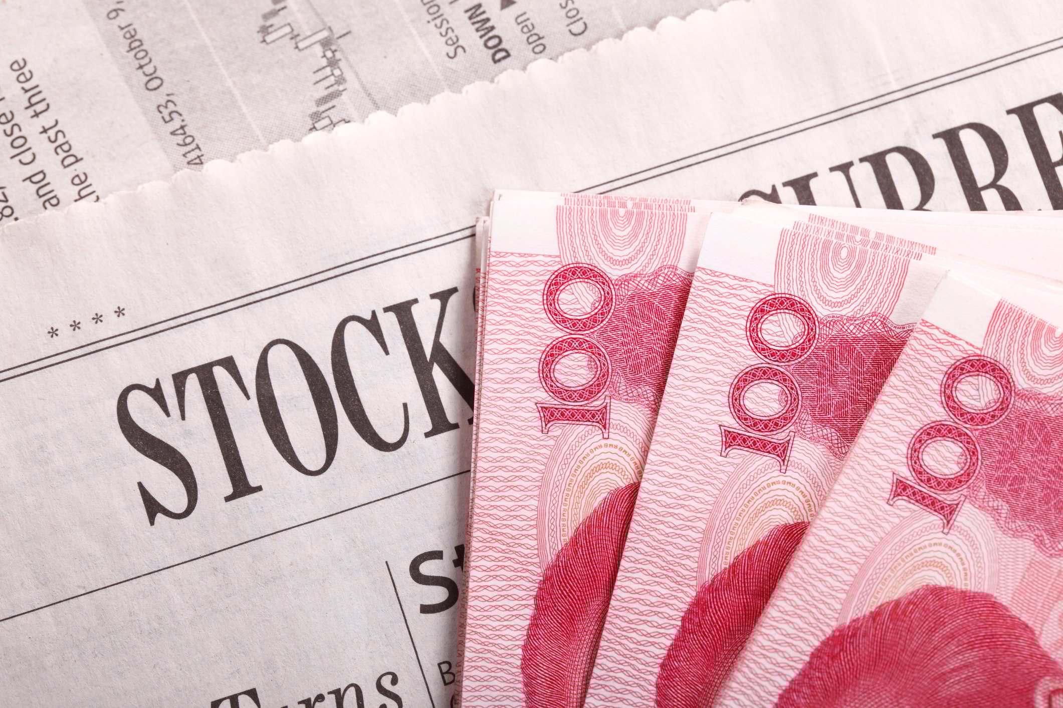Chinese yuan notes lying on a newspaper stocks section.