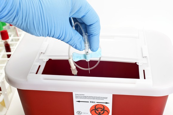 A gloved hand disposing medical waste in a container.