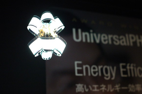 Contemporary lamp made of curved, flexible OLED panels with "UniversalPHOLED" and "Energy Efficient" on a banner in the background.