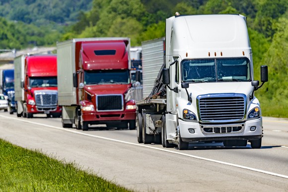 Multiple semi-trucks hauling loads on a highway.
