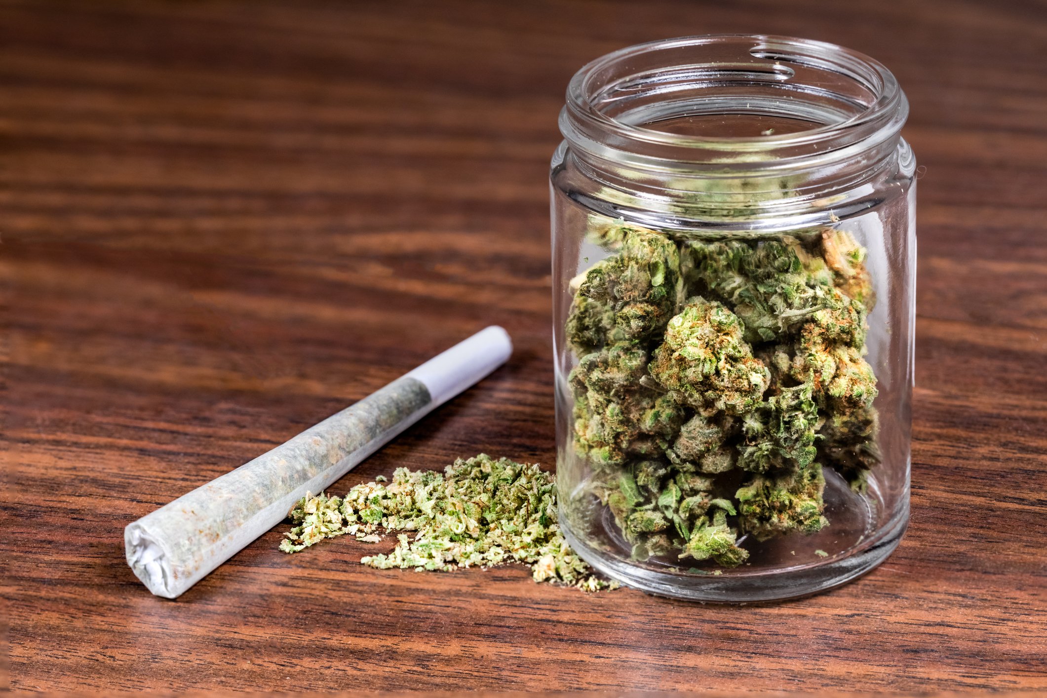 Dried cannabis in a jar, with some seeds and rolling paper on the side.