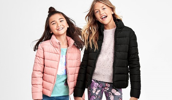 Two smiling girls in jackets, with heads tilted.