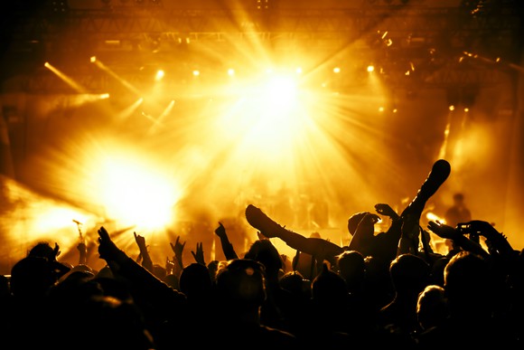 A rowdy crowd at a rock concert, bathed in yellow stage lights.