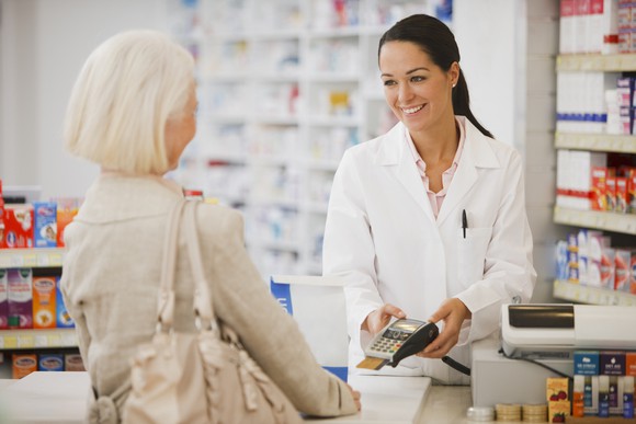 Smiling pharmacist at counter across from older female patient