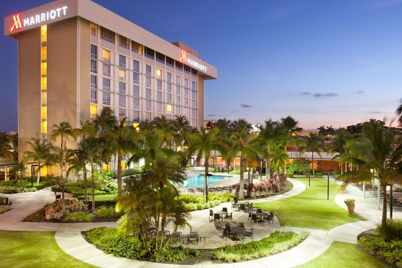 Marriott high rise hotel loverlooking pool and green area with palm trees under a clear dusk sky.