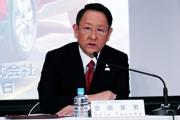 Akio Toyoda is shown seated at a table during a press conference.