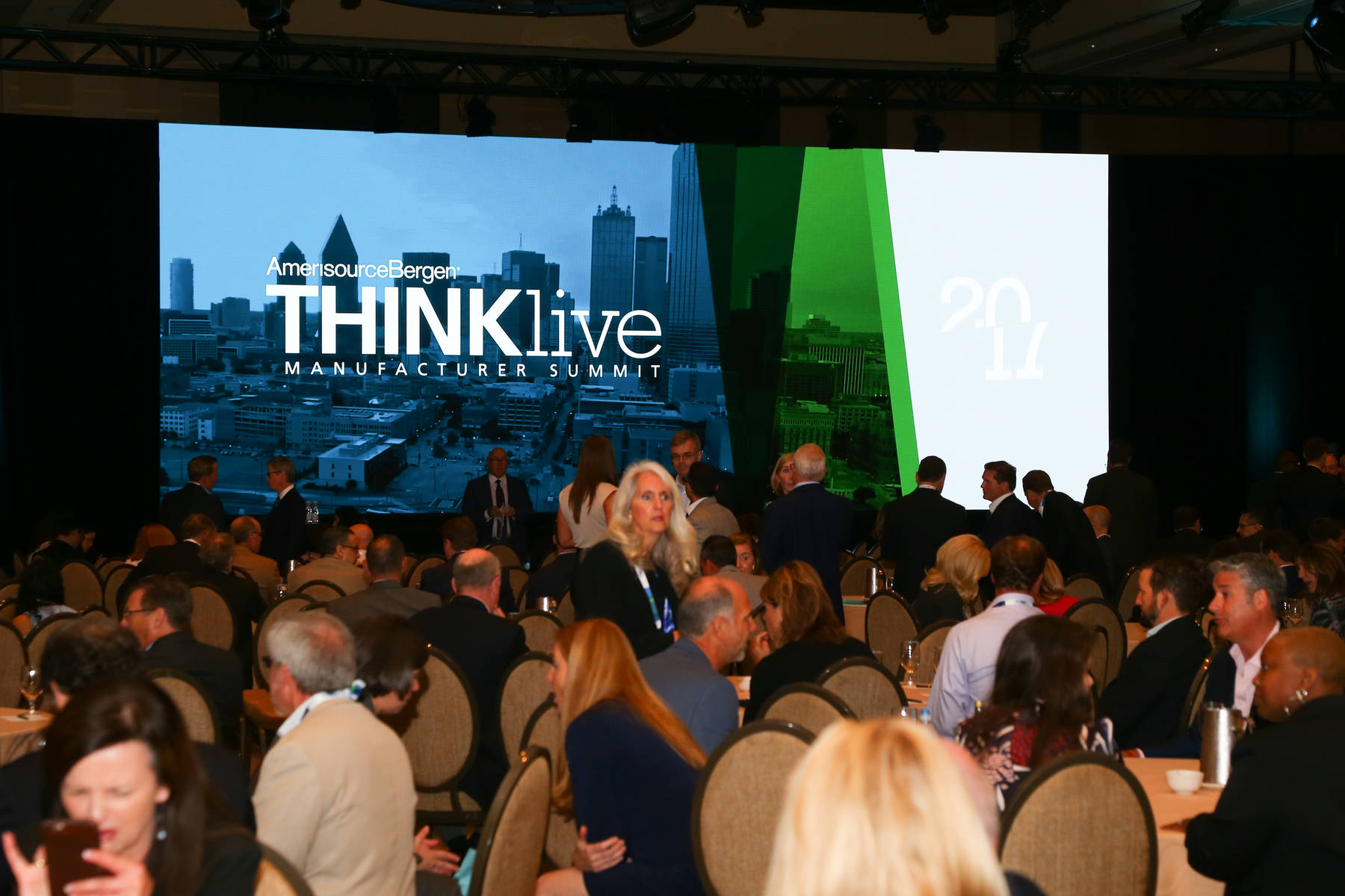 Group of people attending a conference, with a screen showing a graphic for AmerisourceBergen's Thinklive manufacturer summit.