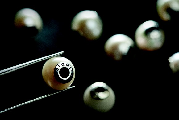 A pair of tweezers lifts a pearl charm.