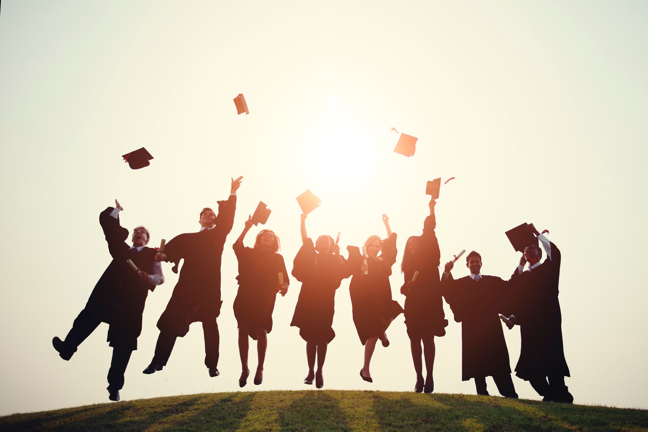 Students wearing graduation robes throw their caps in the air.