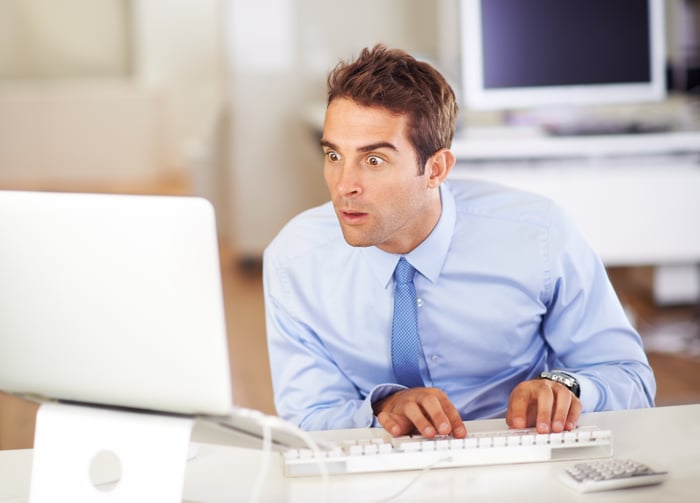 A man in a business shirt and tie with his eyes wide open and a surprised look on his face staring at a computer monitor.