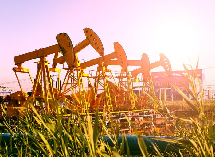 Several oil pumps in a row with a bright sun shining on them.