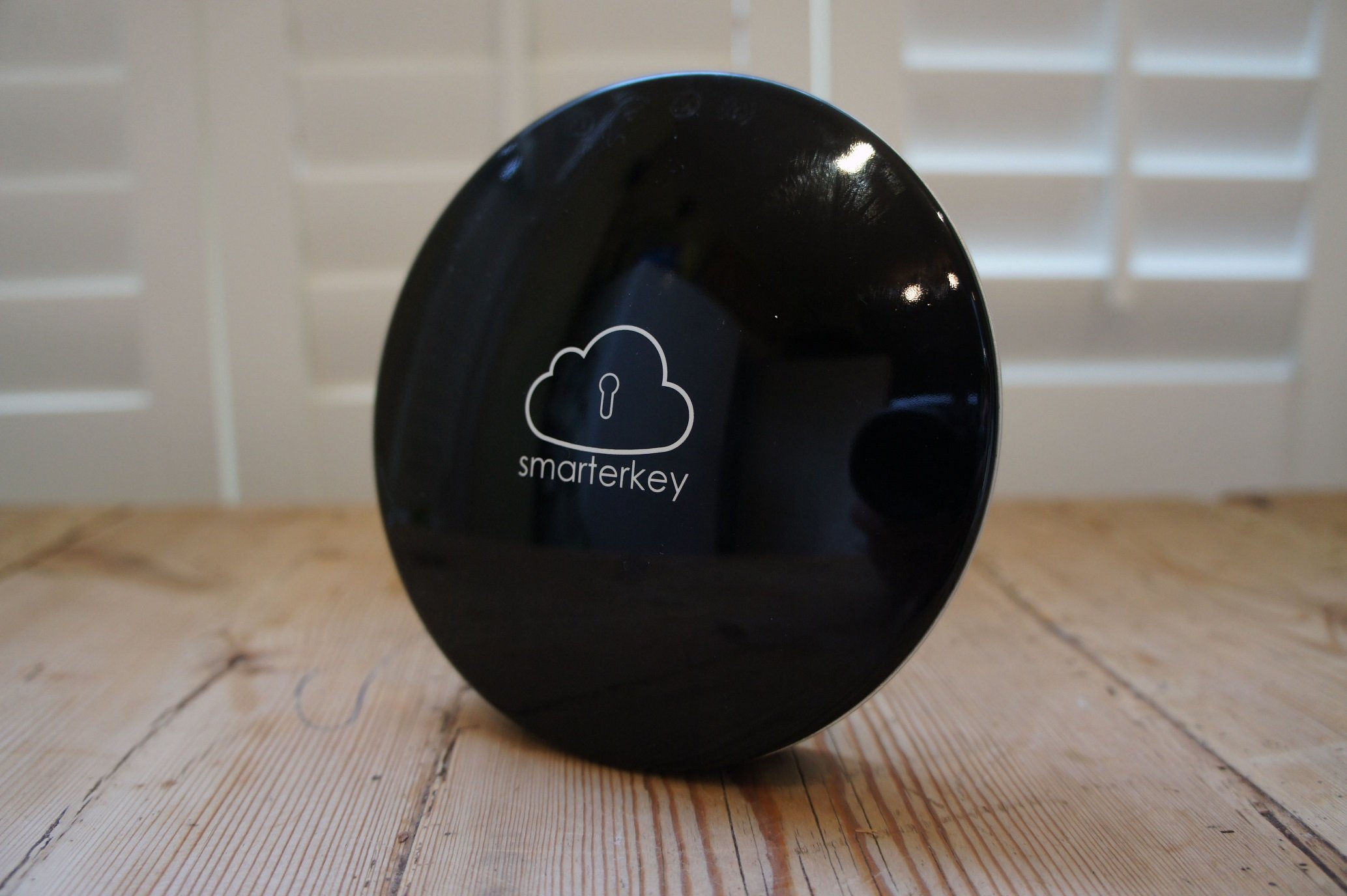 Black Smarterkey device sitting on a wood floor next to window shutters.