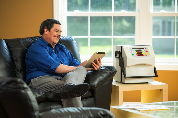 Man in a leather chair looking at a tablet next to a piece of medical equipment.