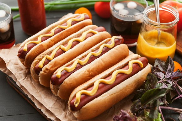 American hot dog with condiments on a dark wooden background.