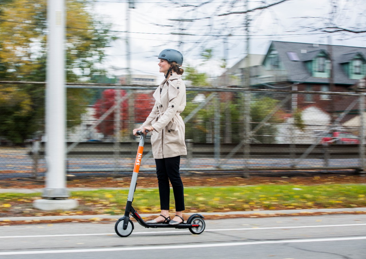 A woman riding a Spin e-scooter in a bicycle lane on a street in Detroit.
