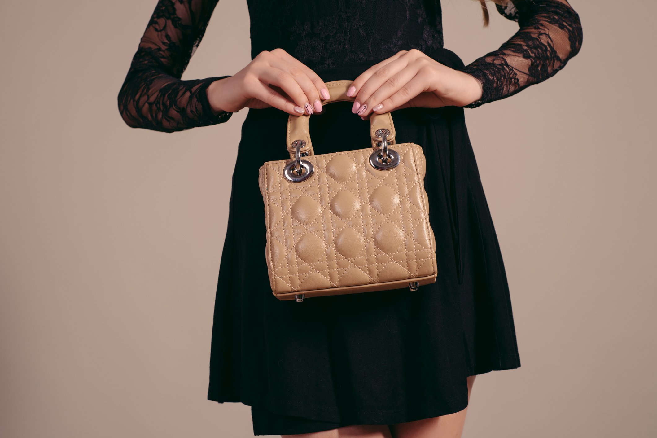 Woman in stylish black dress holding luxury handbag.