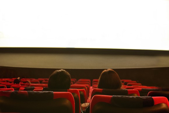 The back of two people's heads in a movie theater, with empty seats around them.