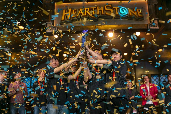 Professional Hearthstone players holding up a trophy with confetti falling as they celebrate a victory at an esport event.