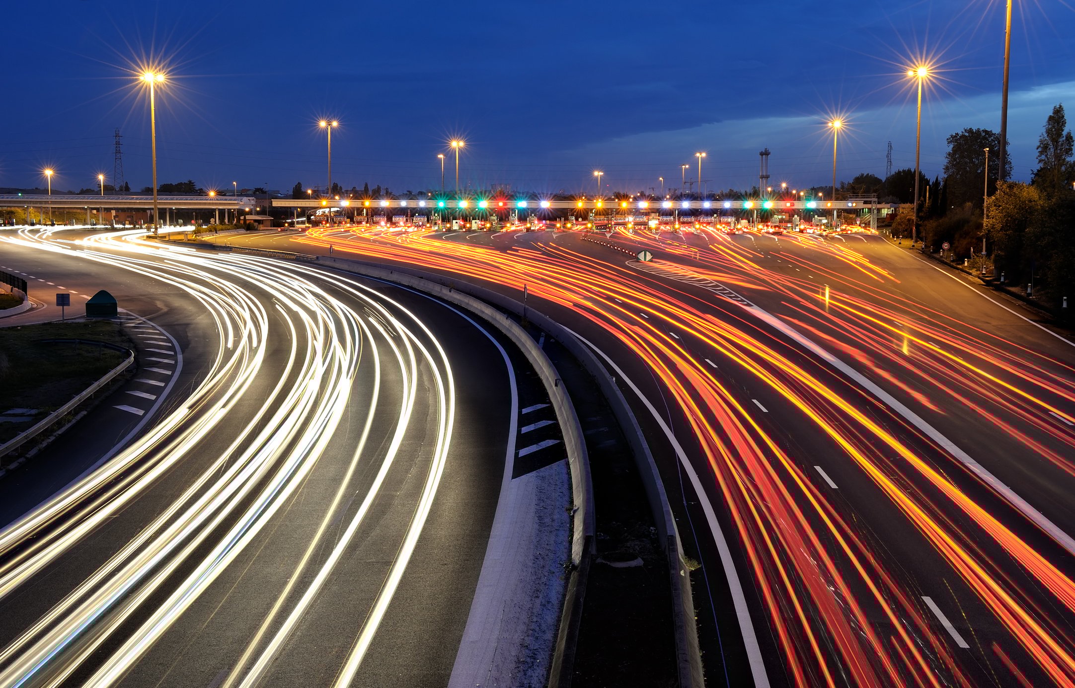 A toll road with traffic blurring at night.