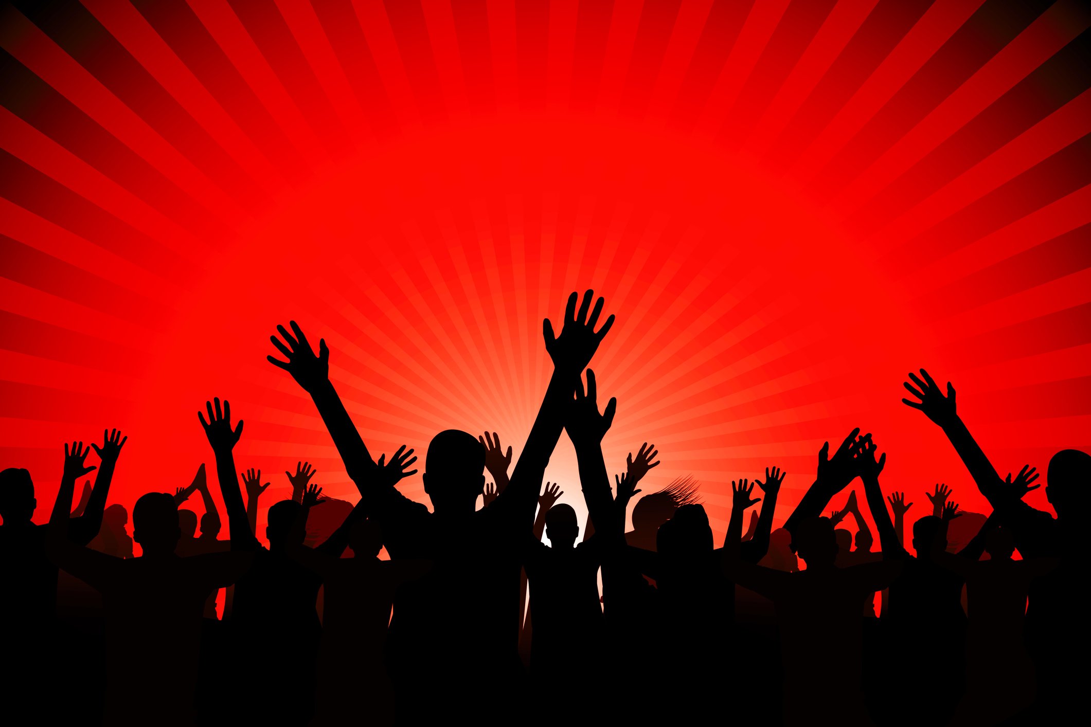A large crowd of people with their hands in the air, silhouetted against a red light in the background.
