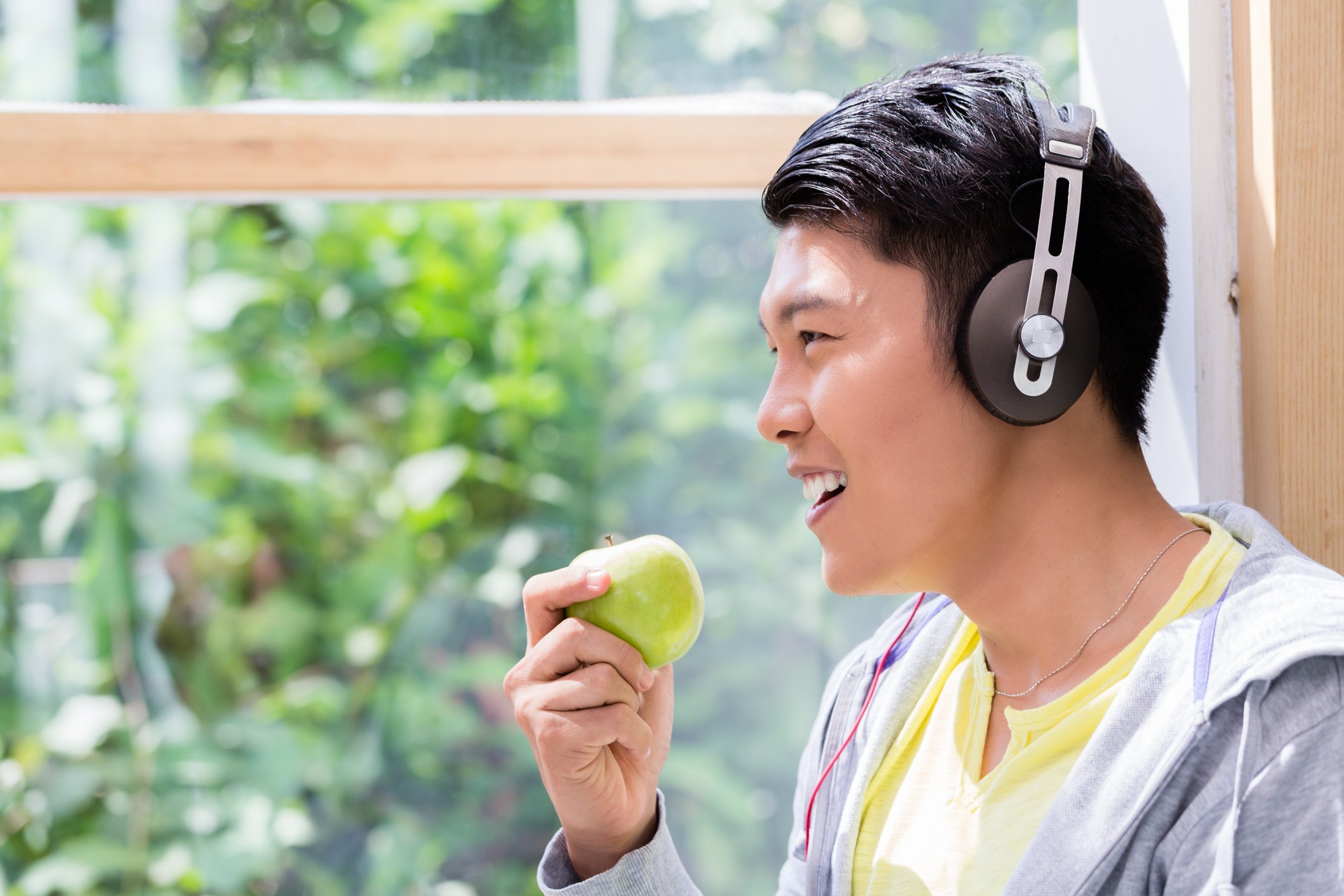 A man wears headphones while eating an apple.