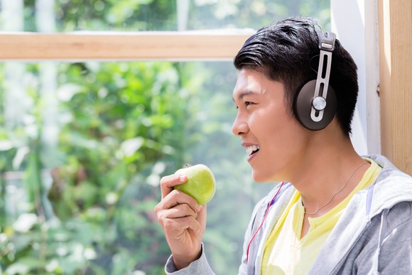 A man wears headphones while eating an apple.
