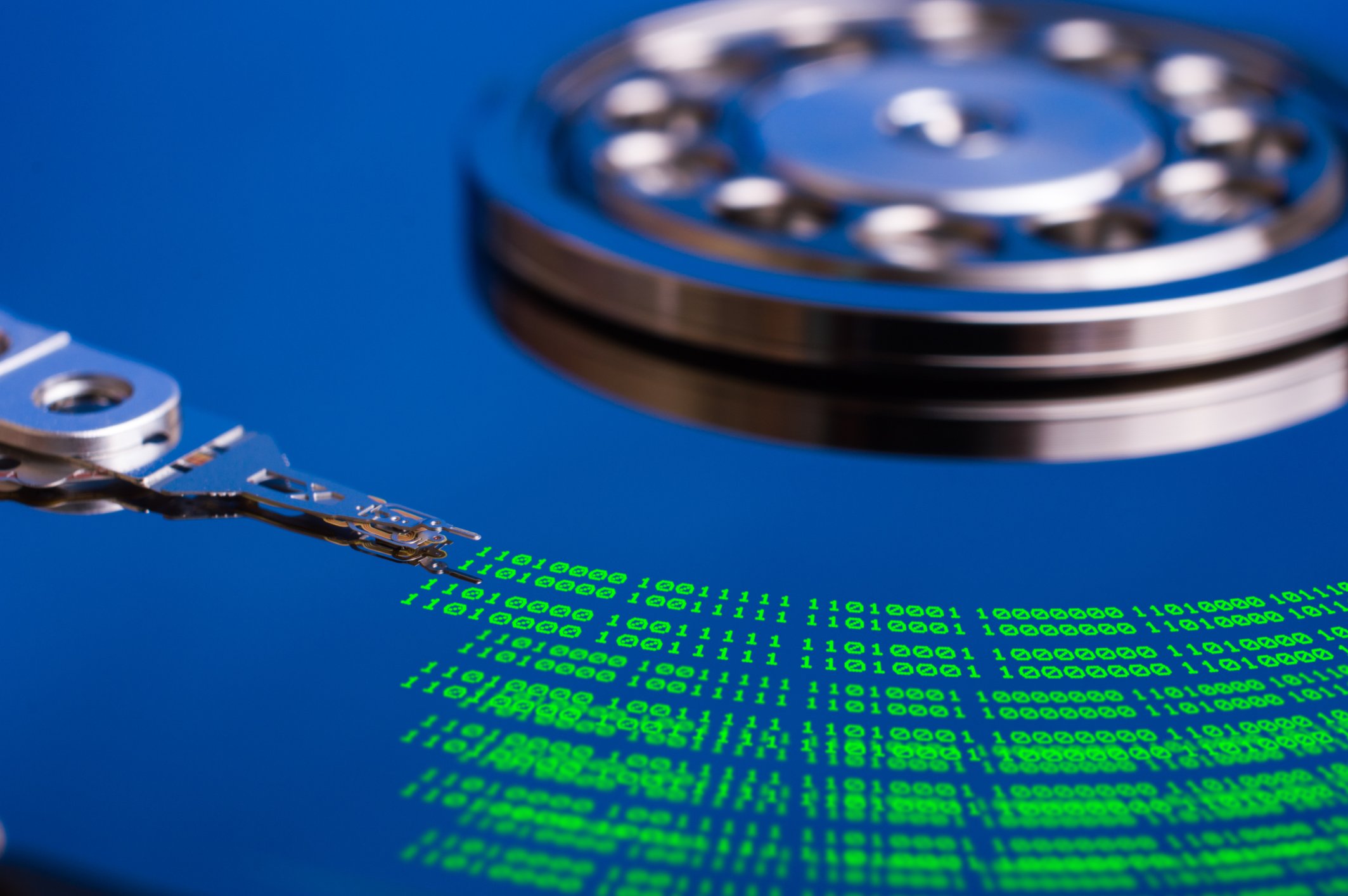 A naked hard drive platter decorated with stripes of green ones and zeroes under the data-reading head.