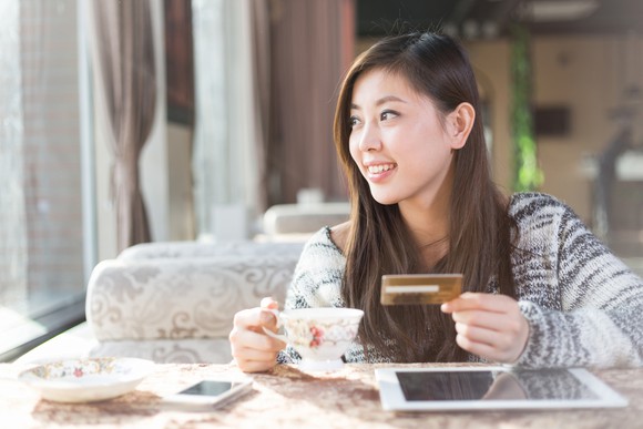 A young woma shops online while drinking tea.