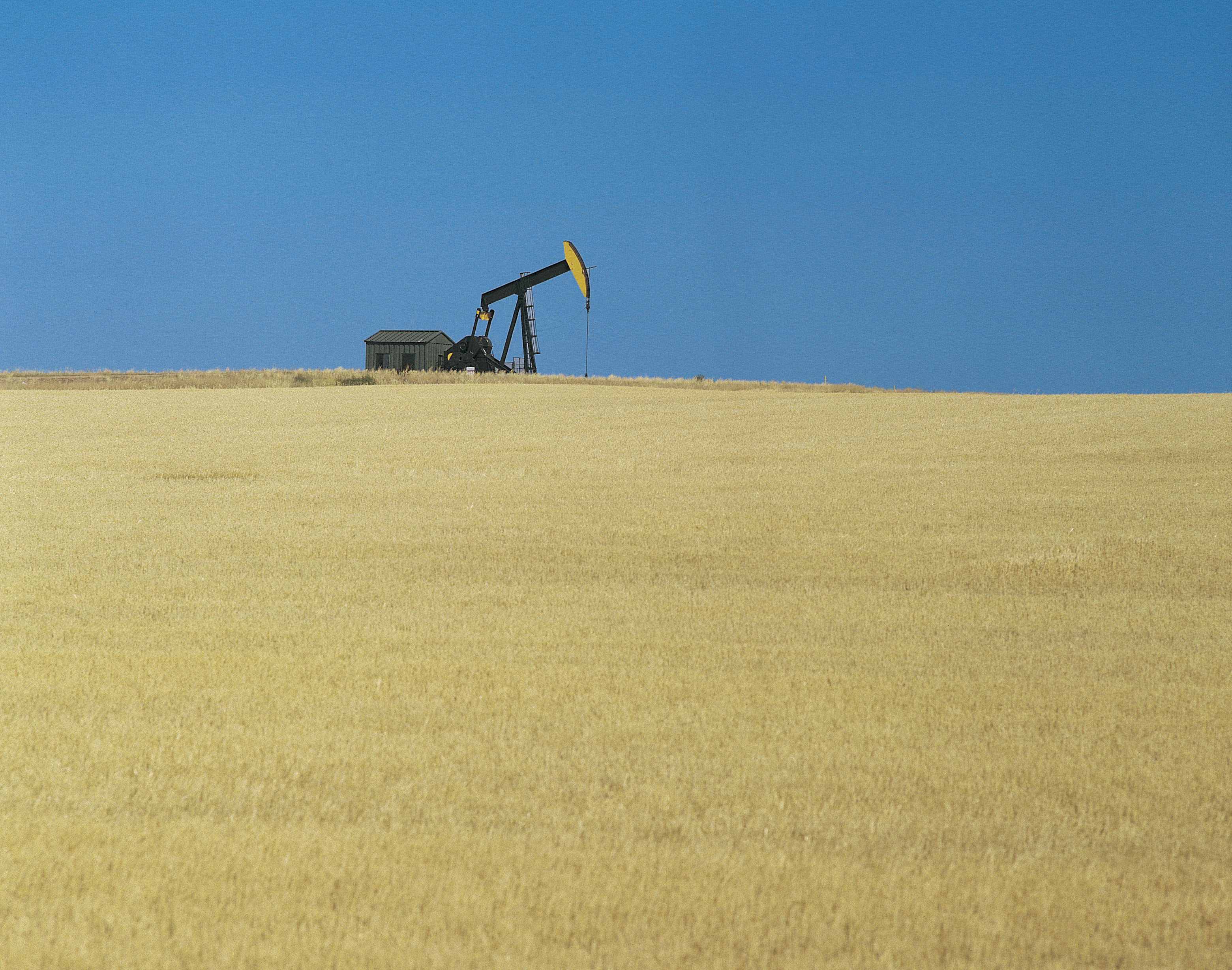 An oil pump on the horizon, with prairie in the foreground and blue sky behind it