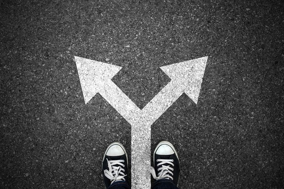 Diverging arrow drawn on pavement, with shoes standing in front of the arrow.