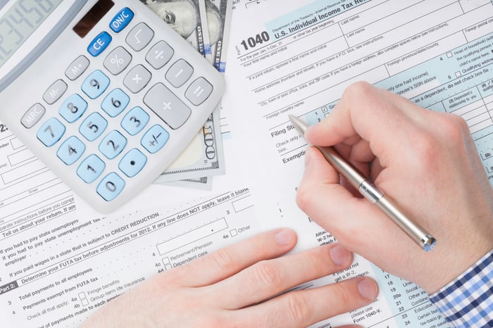 Person filling out a 1040 tax form with calculator and money nearby.